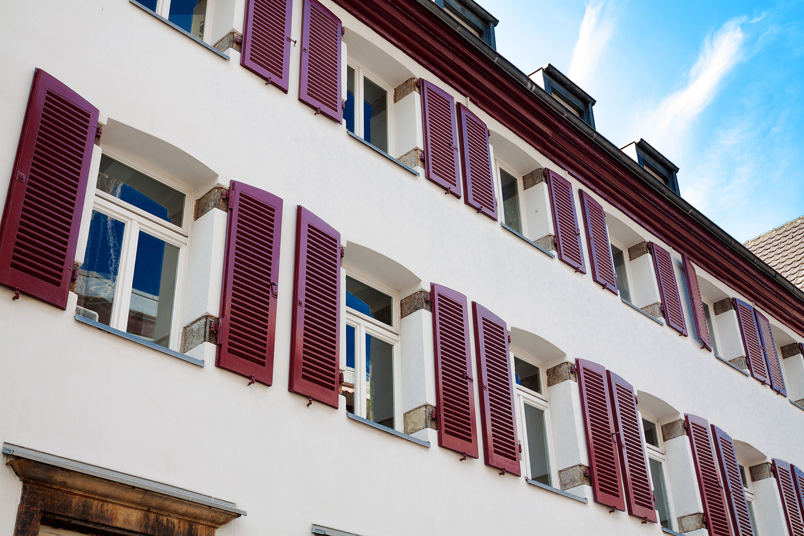 Altbau-Fassade mit weinroten Lamellen-Klappläden